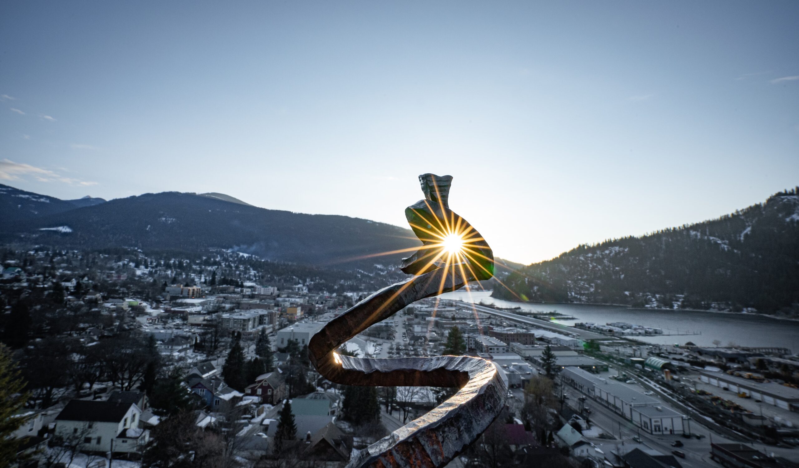 Scenic view of downtown Nelson, BC, tree-lined streets, and stunning mountain backdrop under a clear blue sky.