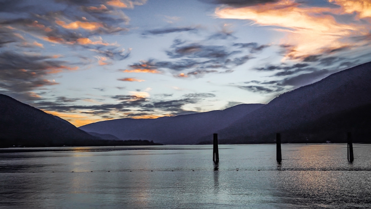 View of Kootenay Lake with pilings marking the safe passage route for boaters, surrounded by serene waters and mountain scenery.