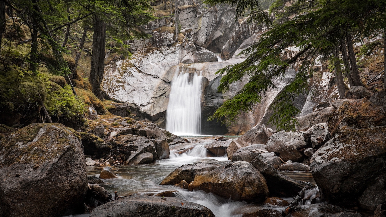 Serene forest scene in the Kootenays, BC, with lush greenery surrounding a cascading waterfall, creating a peaceful, natural atmosphere