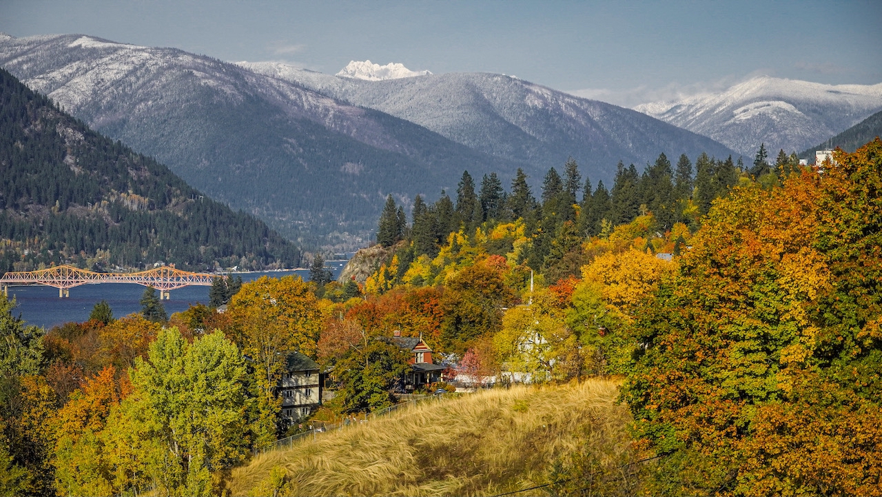 Downtown Nelson, BC, in autumn, with vibrant fall foliage lining the streets and a crisp, golden hue over the town and surrounding mountains