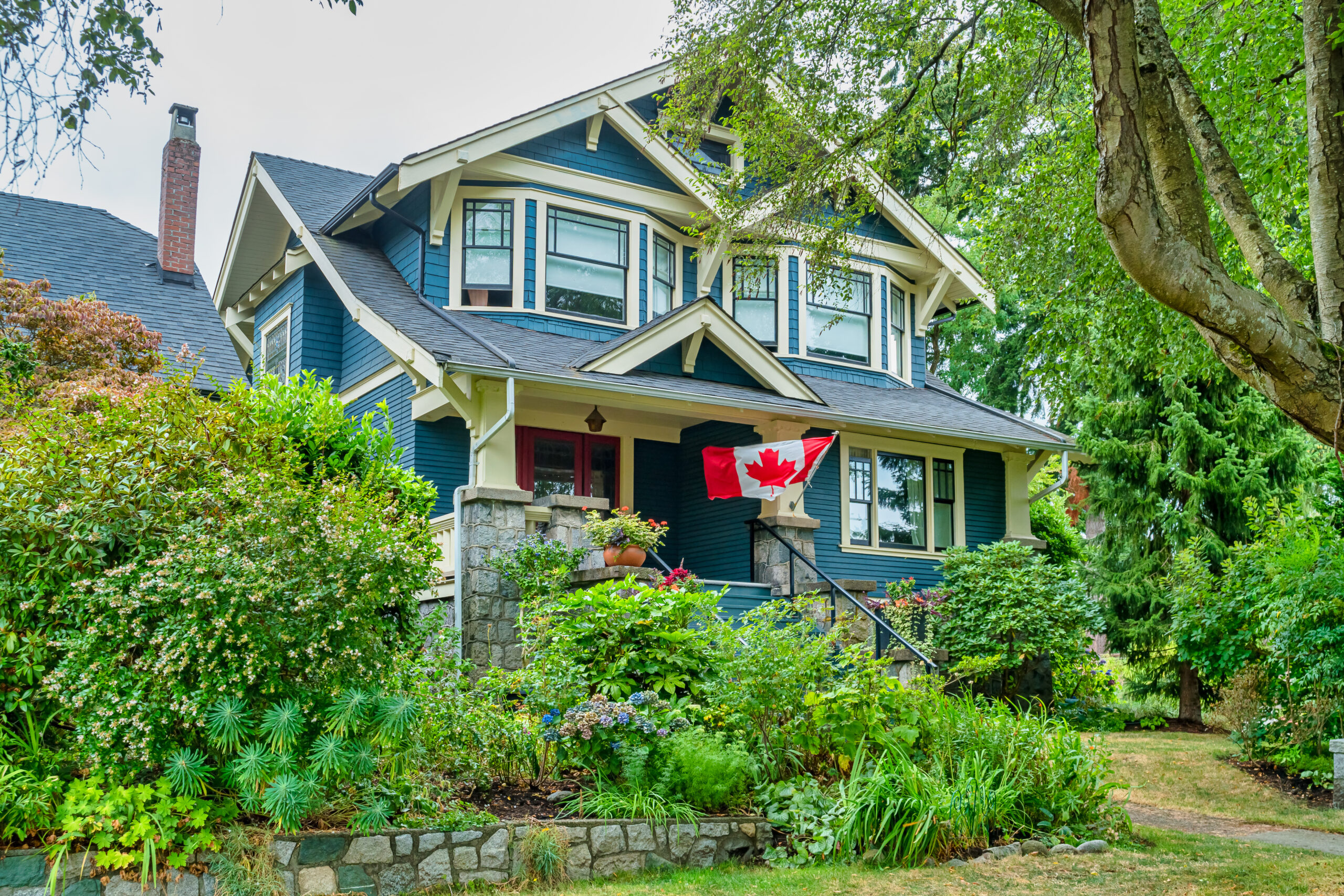 Exterior view of a charming heritage home with classic architectural details, featuring a wraparound porch, ornate wooden trim, and vintage windows, nestled among mature trees and lush greenery."