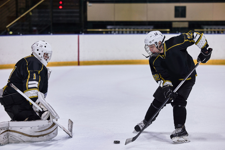 Young hockey player taking a shot on goal against a goalie in blank uniforms during a practice session.