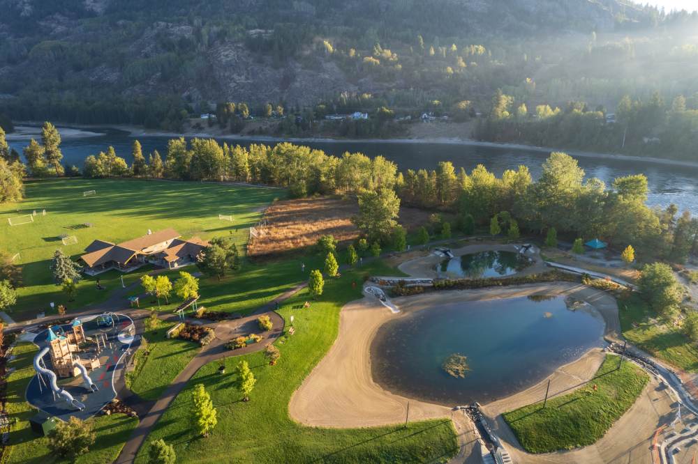 Aerial view of Millennium Park in Castlegar, BC, showcasing green lawns, tree-lined paths, and the Columbia River